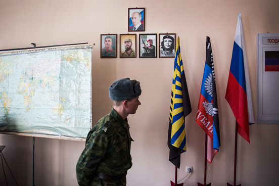 Um rebelde pró-Rússia passa por retratos do presidente russo Vladmir Putin e dos líderes pró-comunismo na sede do Batalhão Kalmius, em Donetsk, Ucrânia. (Foto: Andrew Burton / Getty Images)