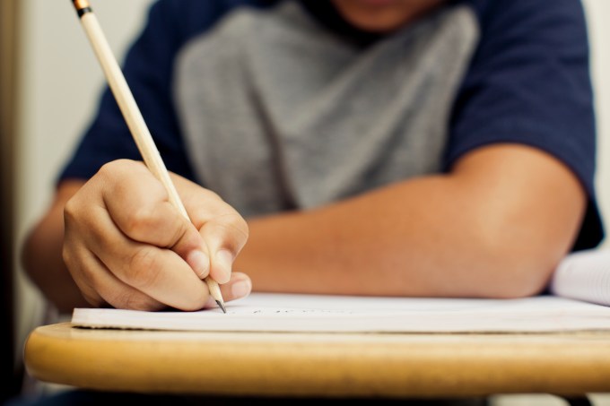 Aluno escrevendo com lápis em uma carteira da escola
