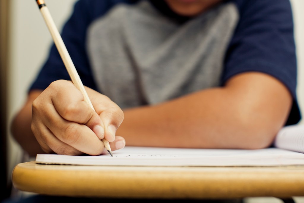 Aluno escrevendo com lápis em uma carteira da escola