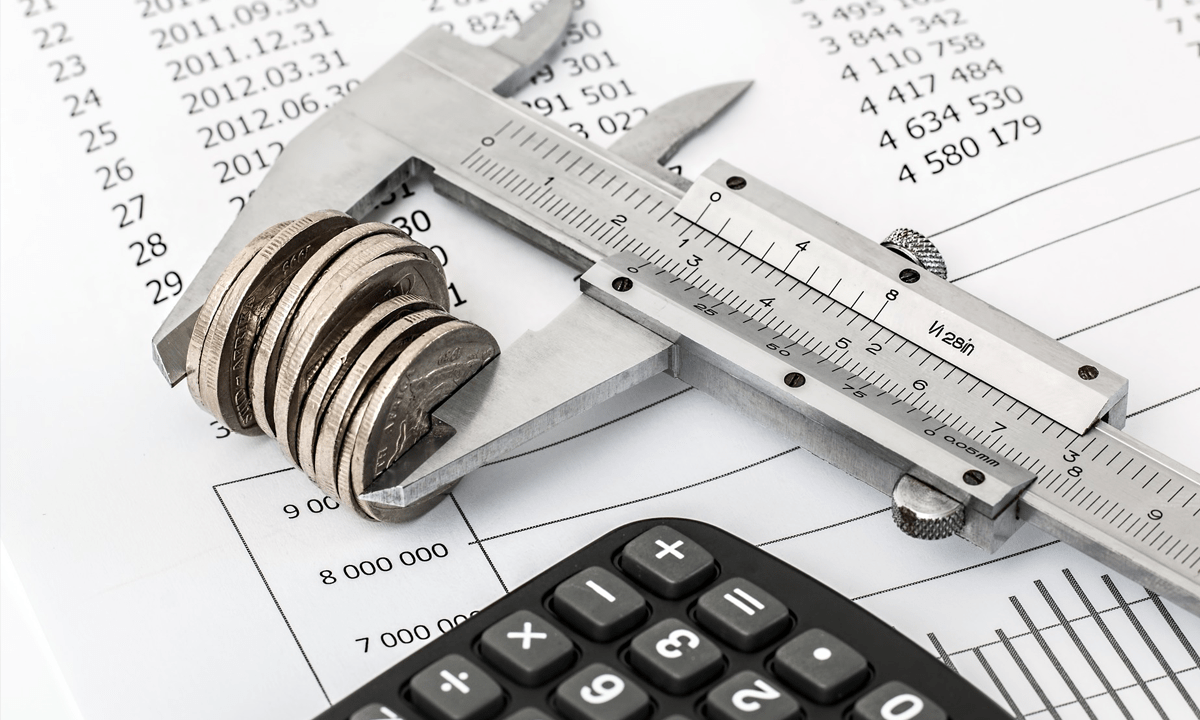 Conjunto de moedas sendo medidas, ao lado de um calculadora e uma tabela de valores.