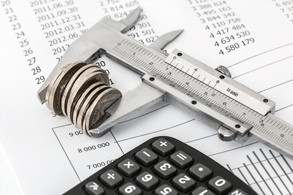 Conjunto de moedas sendo medidas, ao lado de um calculadora e uma tabela de valores.