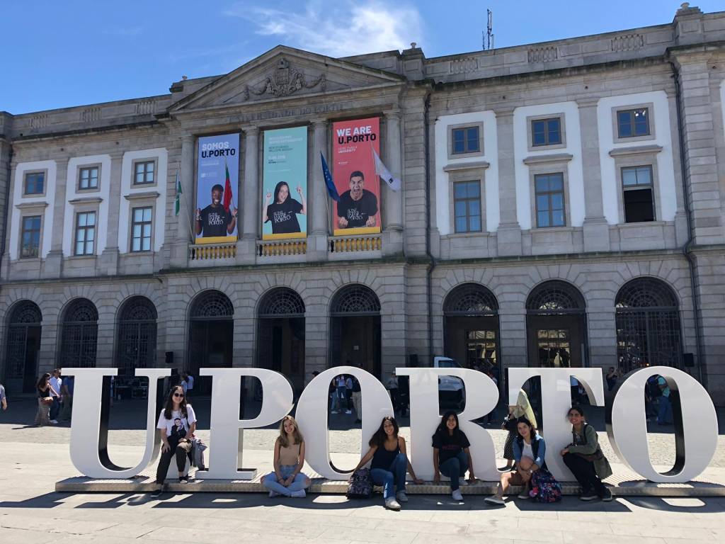 Estudando em Portugal 2 Jovens posam no letreiro da Universidade do Porto, em frente a um dos prédios principais da instituição.