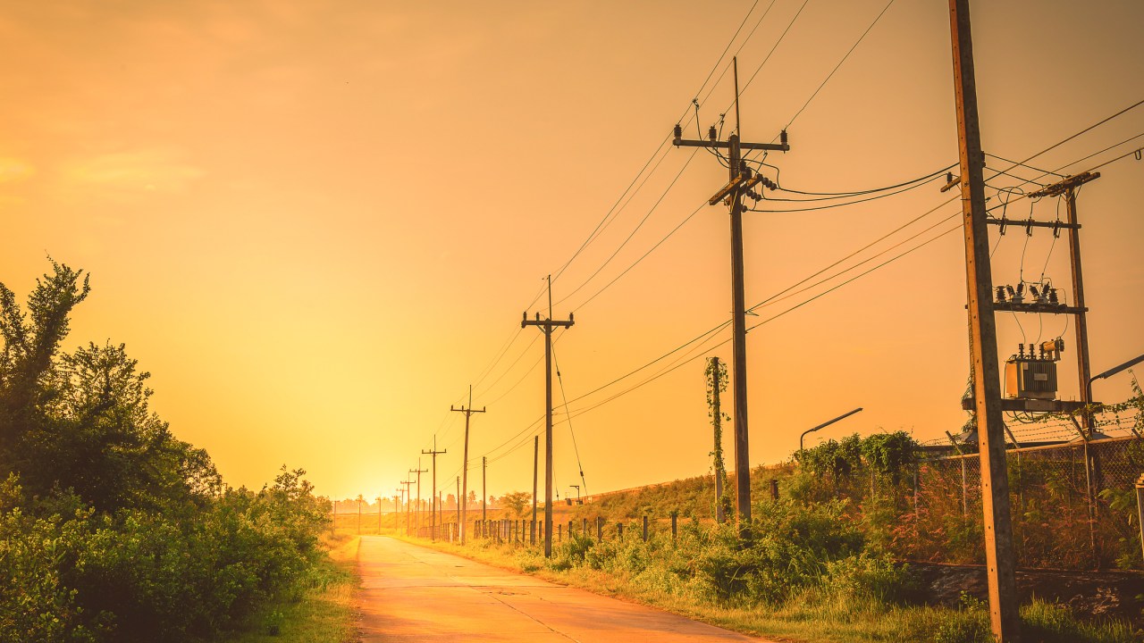 Postes de luz enfileirados em alguma cidade do interior com Sol ao fundo