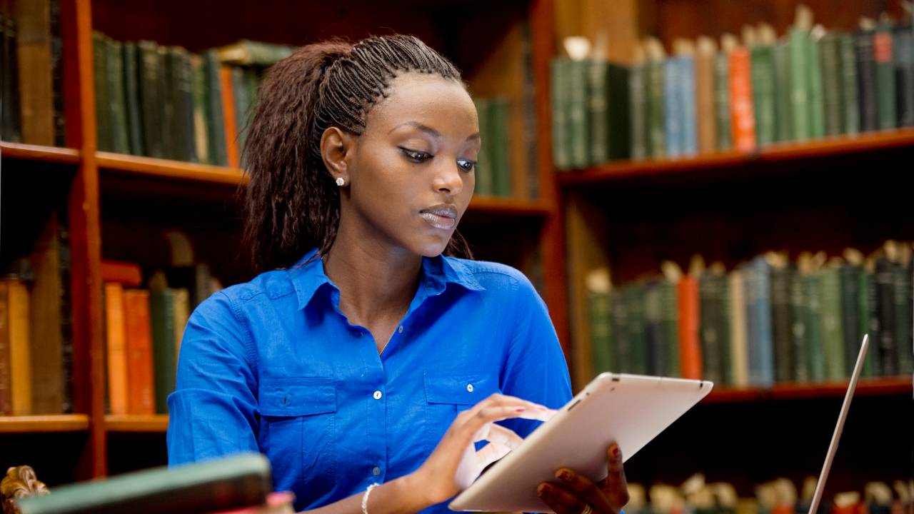 Jovem estuda com tablet e notebook em uma biblioteca