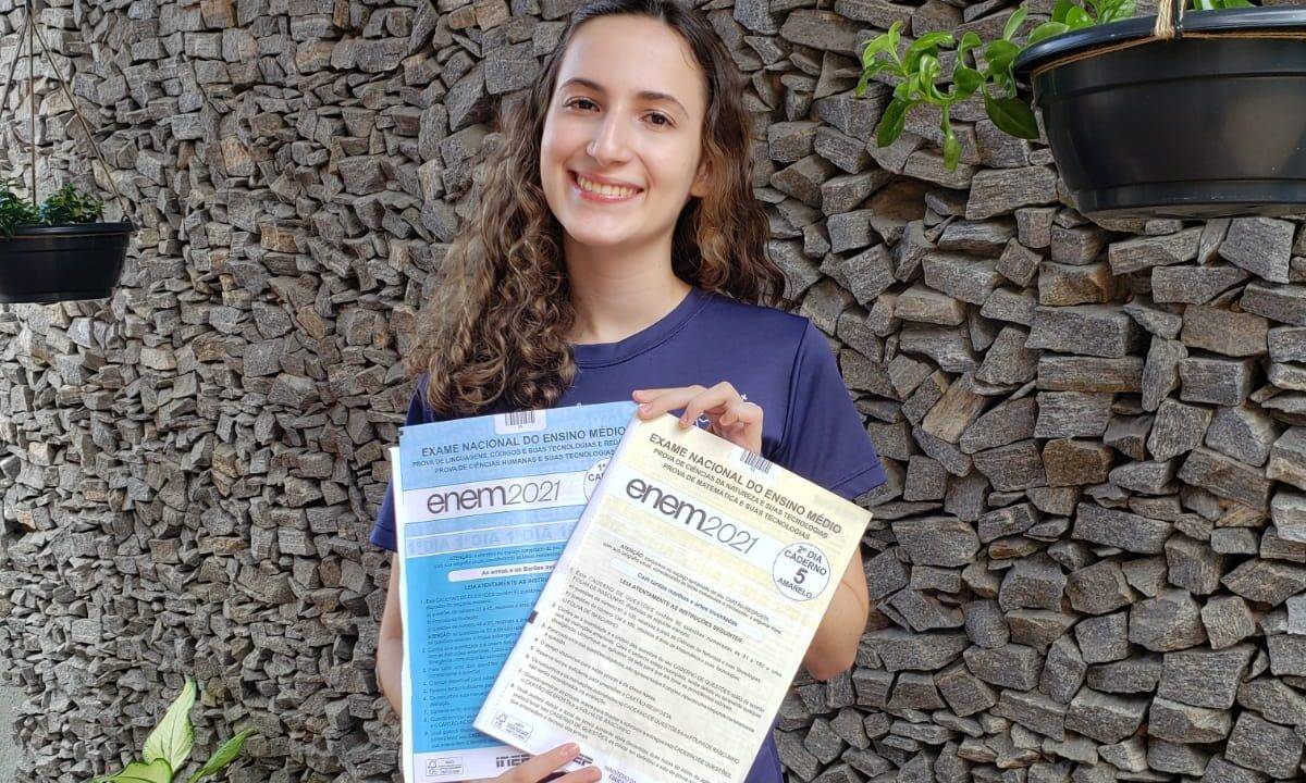 Cássia segurando dois cadernos de prova do Enem 2021