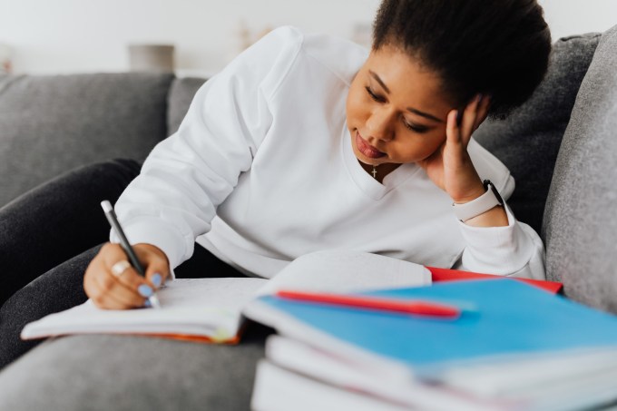 Mulher estudando com livros escrevendo deitada em um sofá