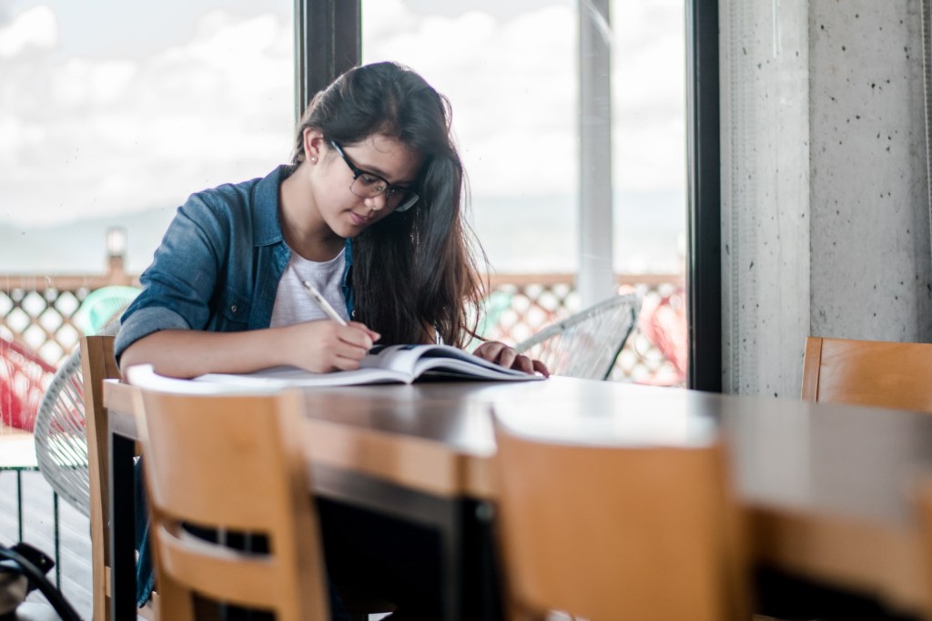 Mulher estudando sozinha na mesa em casa escrevendo em um caderno