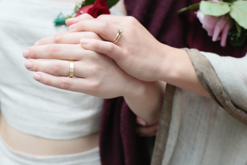 Duas mãos femininas juntas, as duas usam alianças