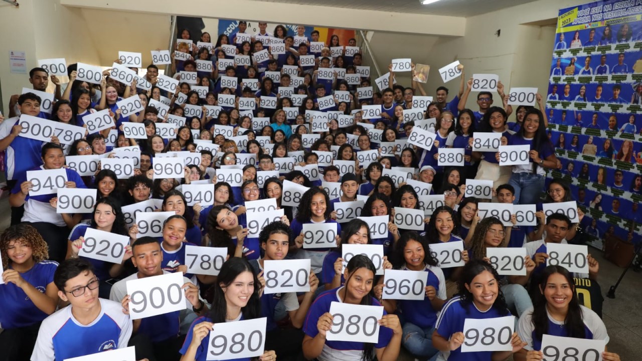 Cerca de 100 estudantes segurando folhas sulfites com suas notas
