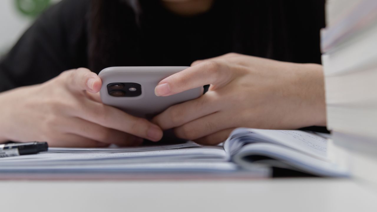menina mexendo no celular em cima dos livros