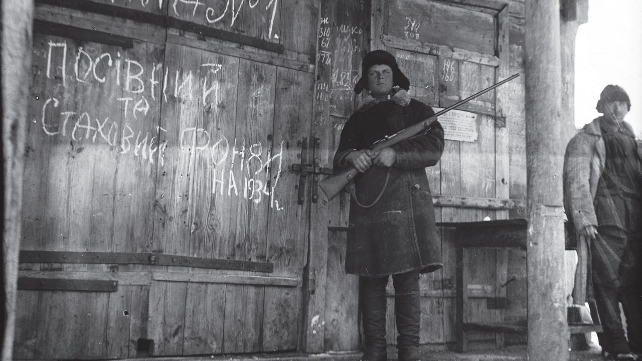 Um membro armado do Komsomol, a organização juvenil do Partido Comunista da União Soviética, protege um celeiro com grãos. Conhecido como Holodomor, o genocídio praticado contra os ucranianos matou milhares de fome
