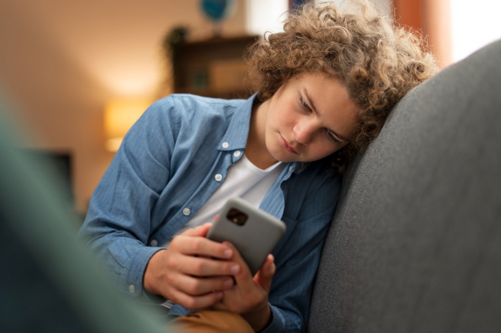 Menino mexeno no celular com semblante triste preocupado