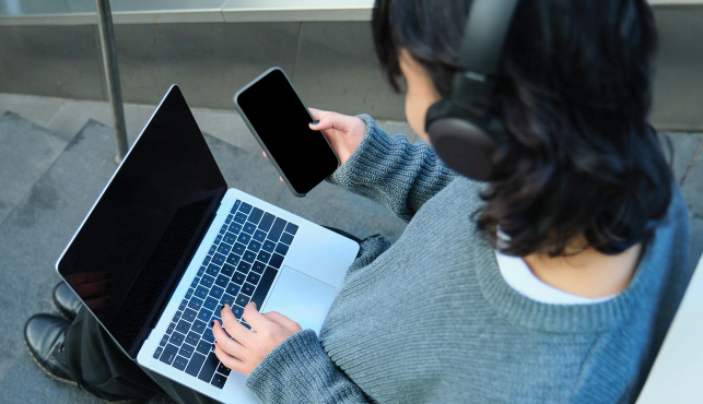 computador-celular-fone jovem mulher sentada mexendo no notebook, celular e usando fone de ouvido